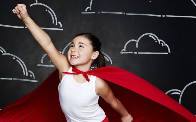 kid with red superhero cape on in superhero one arm up pose